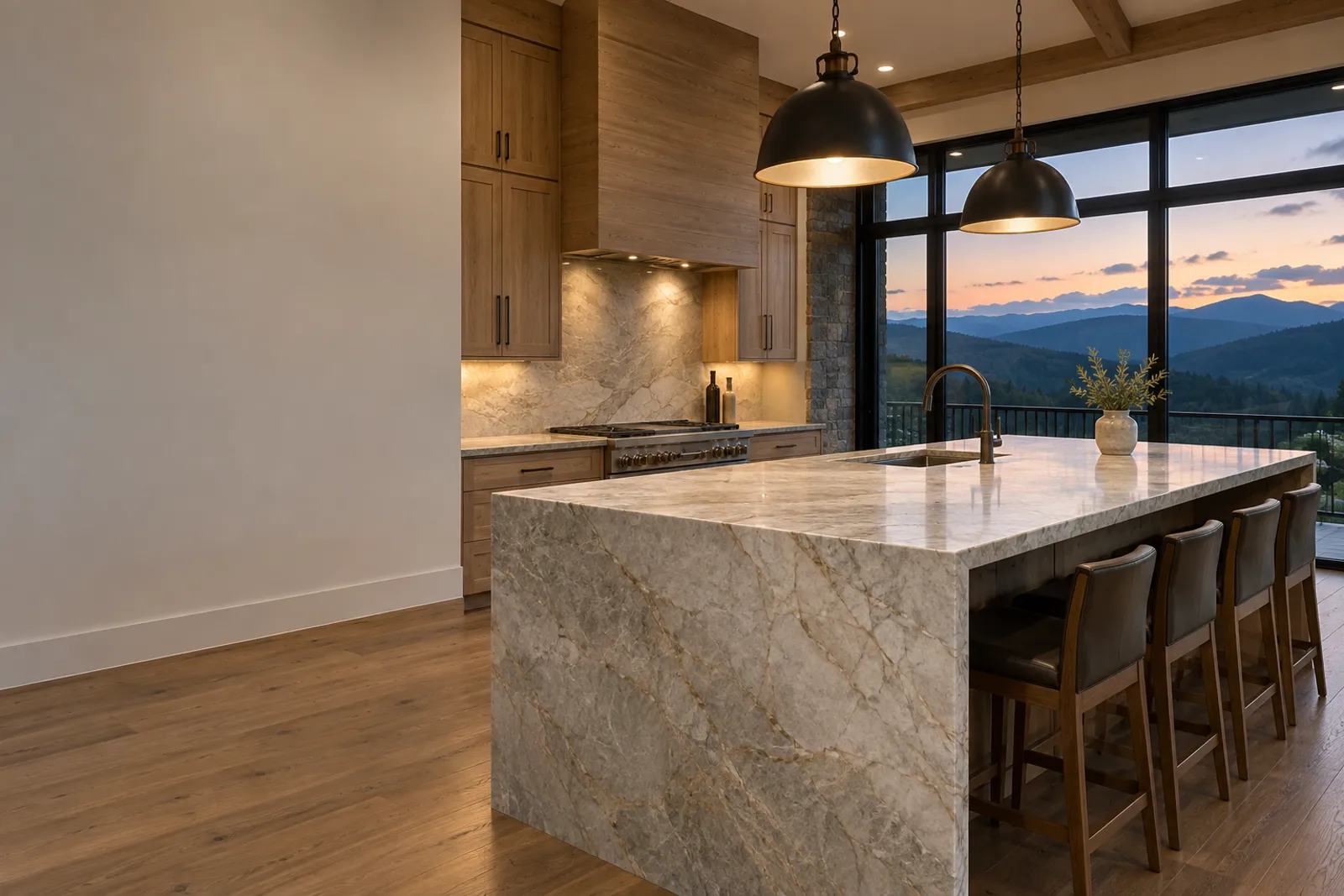 Kitchen with a waterfall-edge quartzite island in grey and gold veining, warm wood cabinets, a stone column, dark leather bar stools and floor-to-ceiling windows onto blue mountain ridges at dusk
